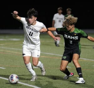 Two soccer players compete for the ball during a night match on a grass field.
