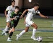 Boys high school soccer match, one player dribbling the ball while others are in pursuit on a grassy field.