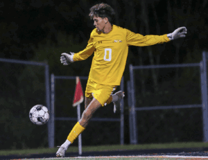 Soccer goalkeeper in yellow uniform making a powerful kick during a night match on the field.