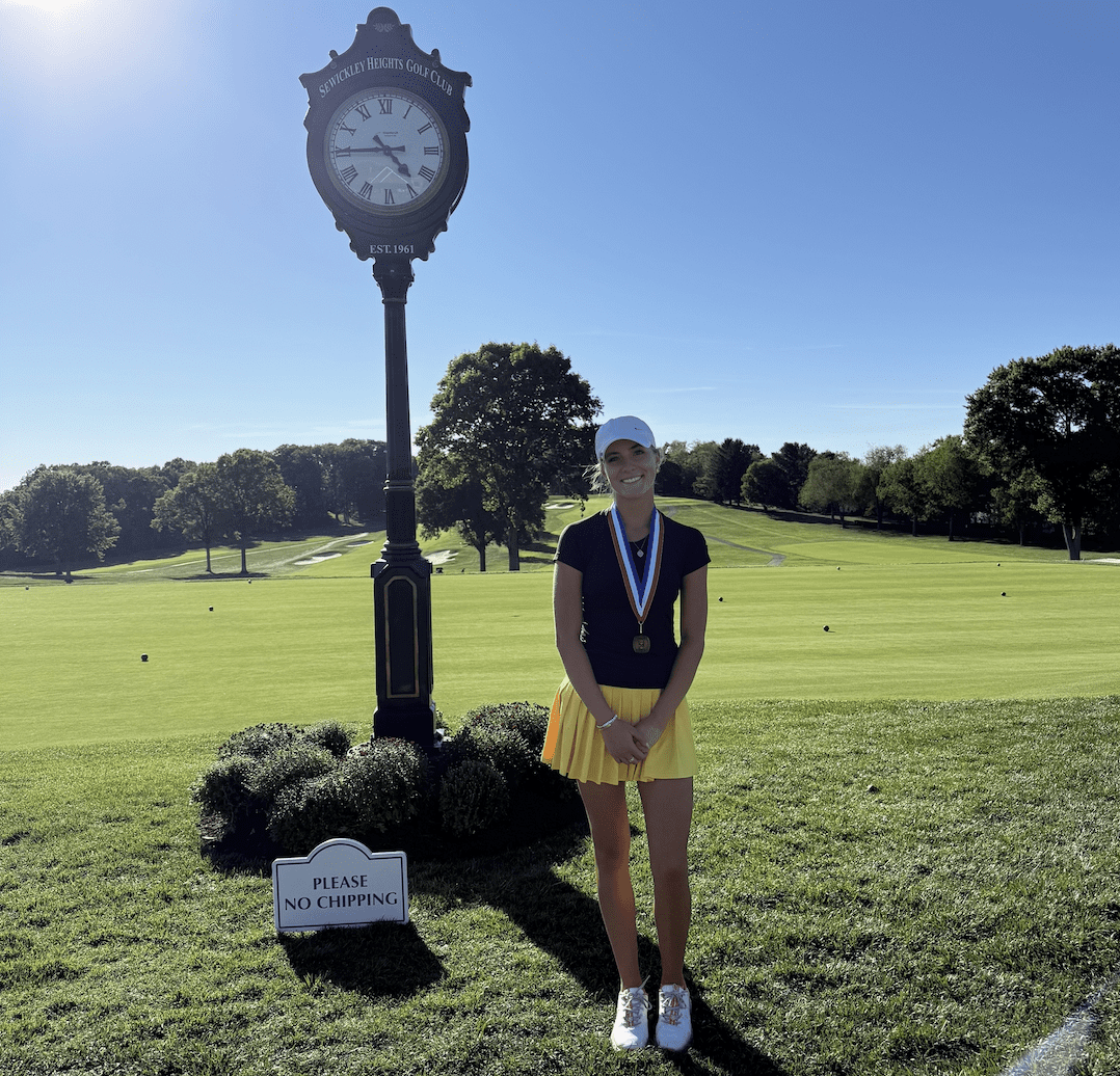 Golfer with medals poses near clock at Sewickley Heights Golf Club. Sunny day on the course.