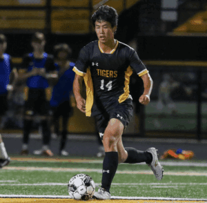 Soccer player in black and yellow uniform dribbles the ball on a field, focused on the game.