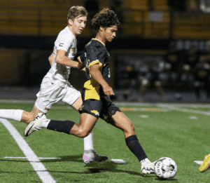 Soccer players competing on a field at night, one in black and yellow, the other in white, both focused on the ball.