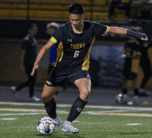 Soccer player in black and yellow jersey dribbling a ball on the field during a night match.