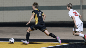 Soccer match action: Player in black sprinting past an opponent in white on the field.