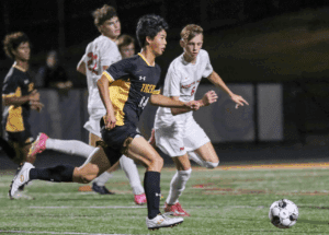 Soccer players in action during a night match, focusing on a player in yellow and black uniform dribbling the ball.