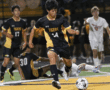 Soccer player in black and yellow uniform kicks ball during intense match.