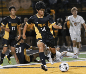 Soccer player in black and yellow uniform kicks ball during intense match.