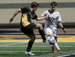 Two soccer players in action during a night match on a green field.