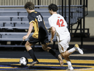 Two soccer players in action on the field, one in black and yellow, the other in white, during a night match.