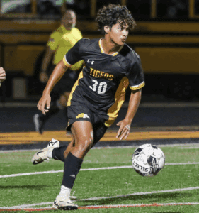 Soccer player in black uniform dribbling ball on the field during a night game.