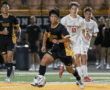 Soccer player dribbles ball during a high school match, with teammates and opponents in pursuit on the field.