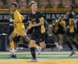 Soccer players in black and yellow uniforms celebrating on the field at night game.