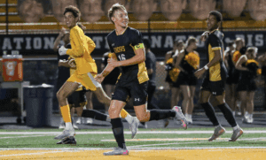 Soccer players in black and yellow uniforms celebrating on the field at night game.