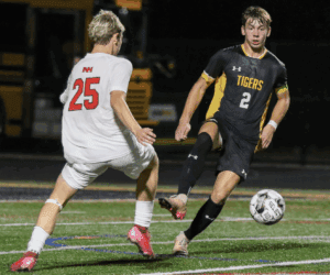 Two soccer players in action during a night match, one in black, the other in white, on a grass field.