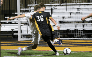 Soccer players in intense game action, number 36 kicking ball towards goal on a vibrant field.