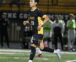 Soccer player in black and yellow jersey running during night match on field.