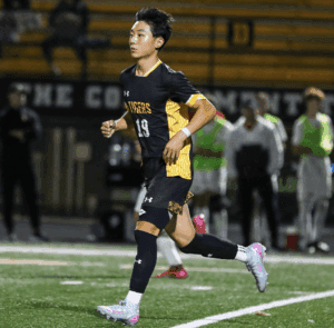 Soccer player in black and yellow jersey running during night match on field.