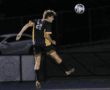 Soccer player in mid-air, number 20, heads the ball during a night match, wearing a black and yellow uniform.