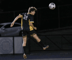 Soccer player in mid-air, number 20, heads the ball during a night match, wearing a black and yellow uniform.