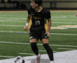 Soccer player in black jersey dribbles ball during night game on field.