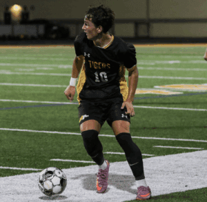 Soccer player in black jersey dribbles ball during night game on field.