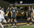 Soccer player attempts a header during a match, surrounded by teammates and opponents on a field at night.