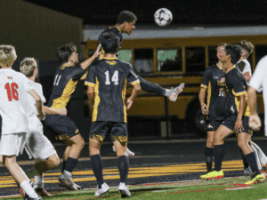 Soccer player attempts a header during a match, surrounded by teammates and opponents on a field at night.