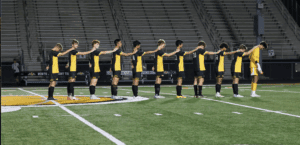 Soccer team lining up on the field at night, wearing black and yellow uniforms with a stadium in the background.