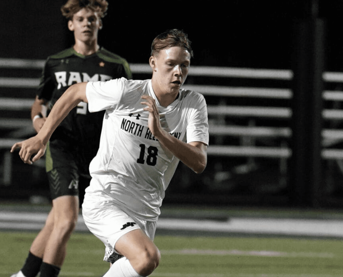 Soccer player in action during a night match, wearing a white jersey with number 18, running past an opponent.