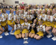 Cheerleading team in yellow uniforms celebrates with a trophy at a competition.
