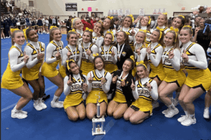 Cheerleading team in yellow uniforms celebrates with a trophy at a competition.