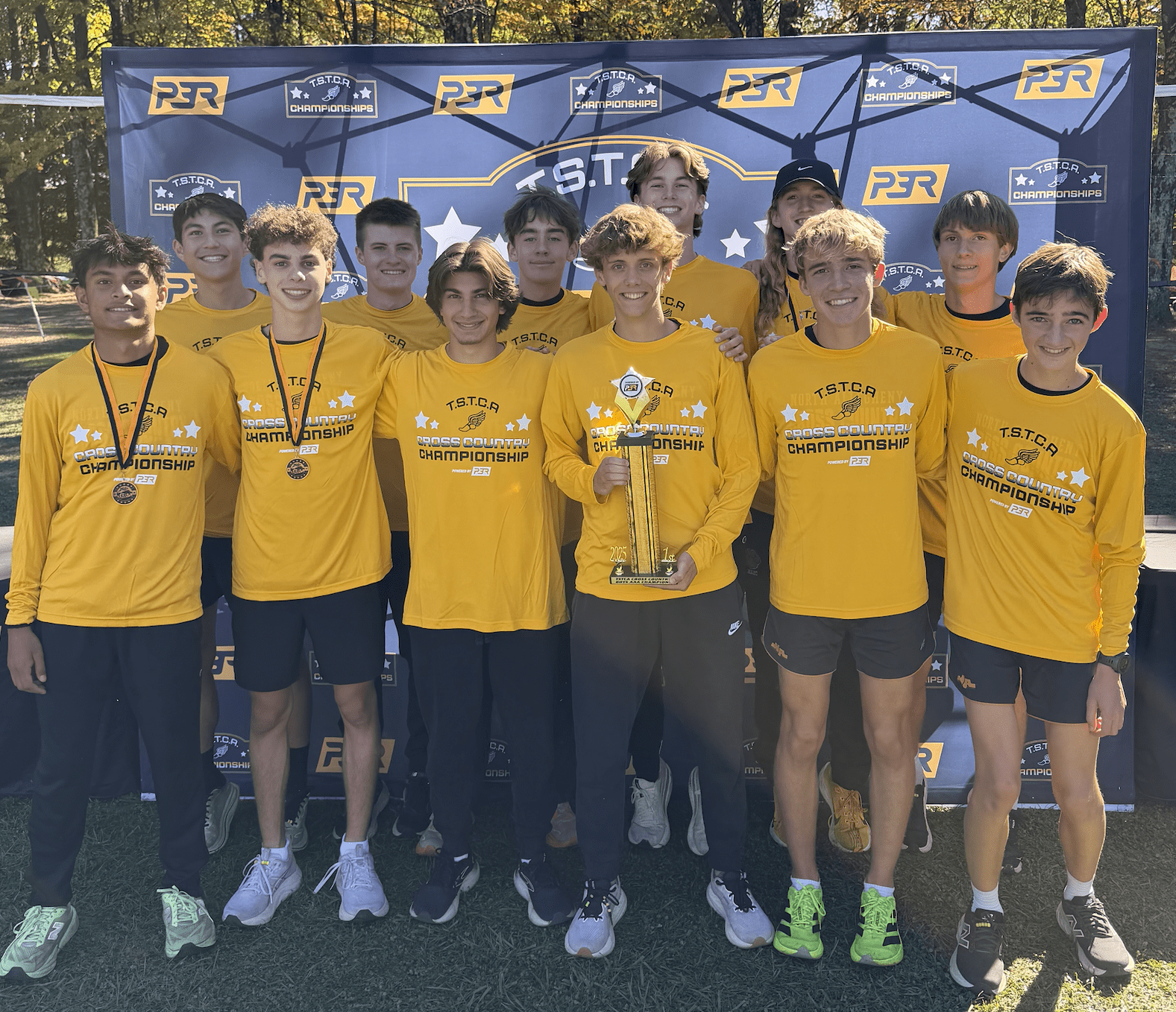 Team celebrates winning cross-country championship, holding trophy in matching yellow shirts at outdoor event.
