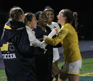 Soccer players celebrate joyfully on the field at night, embracing and laughing after a victorious match.