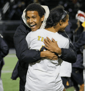Two people celebrating and hugging on a sports field, both smiling joyfully.