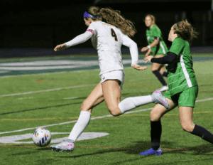 Soccer player in white jersey kicking ball during intense match on green field at night.