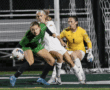 Soccer players compete intensely near goalpost during match, focused on ball control and defense strategy.