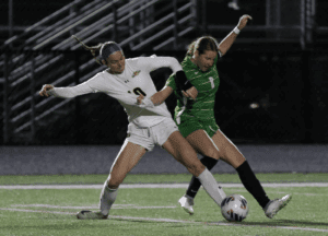 Girls' soccer match action, players competing for ball on field at night.