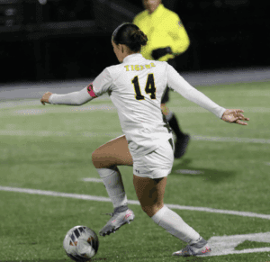 Soccer player in white jersey number 14 dribbling ball during a night match on green field.