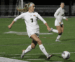 Soccer player in white jersey kicking ball during a night match on green field.