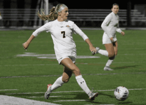 Soccer player in white jersey kicking ball during a night match on green field.