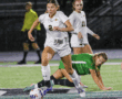 Soccer player dribbling the ball on a rainy field during a competitive match.