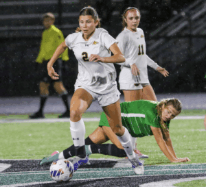 Soccer player dribbling the ball on a rainy field during a competitive match.
