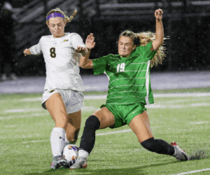 Soccer players in action, one in white and one in green, competing for the ball on a rainy field.