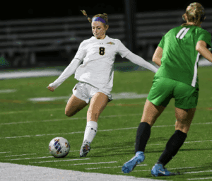 Soccer player in white jersey kicking ball during intense night match on grass field.