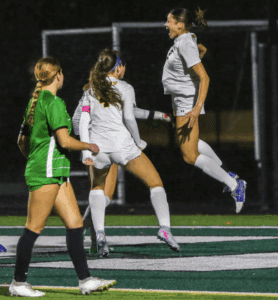 Soccer players in action, jumping and celebrating a goal on the field at night.