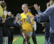 Soccer goalkeeper in yellow jersey high-fives teammates on the field at night, celebrating victory.