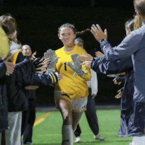 Soccer goalkeeper in yellow jersey high-fives teammates on the field at night, celebrating victory.
