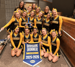 Cheerleading team celebrates winning the regional division for 2025-2026 with trophy and banner indoors.