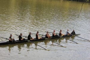 Team of women rowing on a calm lake, coordinated in a sleek racing boat.
