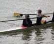 Team rowing in a race, coxswain guiding while athletes row on a river, boat with number 166.